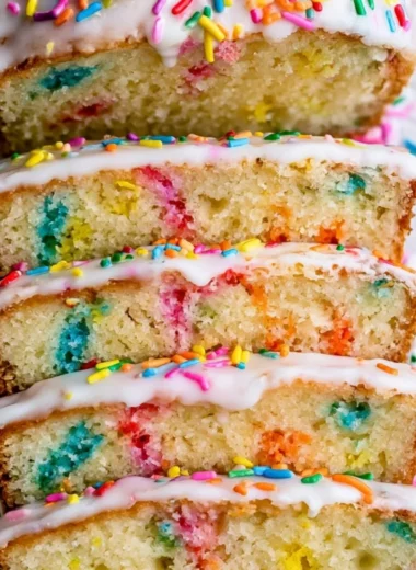 A slice of Funfetti Pound Cake topped with colorful sprinkles on a white plate.