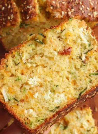 Slice of one bowl cheesy zucchini bread on a wooden cutting board.