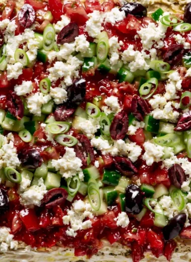 Greek-inspired layered dip with Mediterranean ingredients in a colorful presentation.
