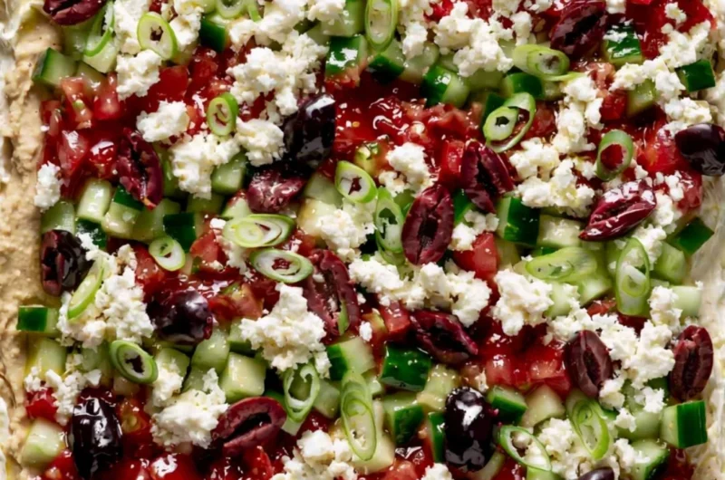 Greek-inspired layered dip with Mediterranean ingredients in a colorful presentation.