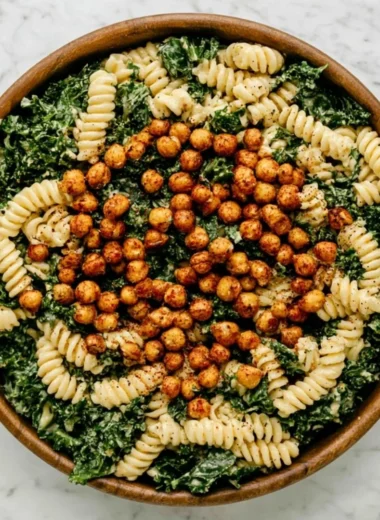 A vibrant Kale Caesar Pasta Salad topped with croutons and parmesan cheese.